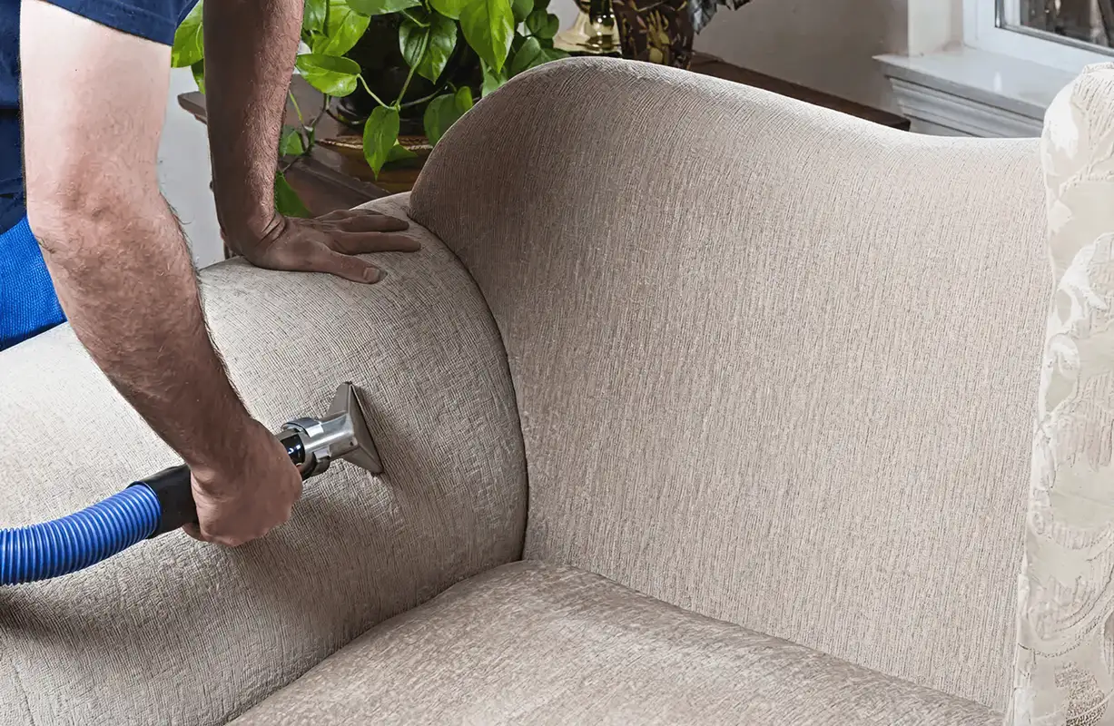 Professional upholstery cleaner deep-cleaning a fabric sofa with a handheld extraction tool and hose, Boca Raton, FL.